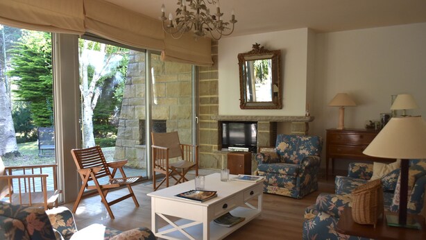 A living room with a fireplace, a television, and a large window overlooking a garden. - rent house in St Briac near golf and beaches, 9 people (Saint-Briac-sur-Mer)