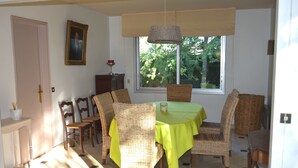 A dining room with wicker chairs and a table covered with a green tablecloth. There is a window with a view of trees outside. - rent house in St Briac near golf and beaches, 9 people (Saint-Briac-sur-Mer)