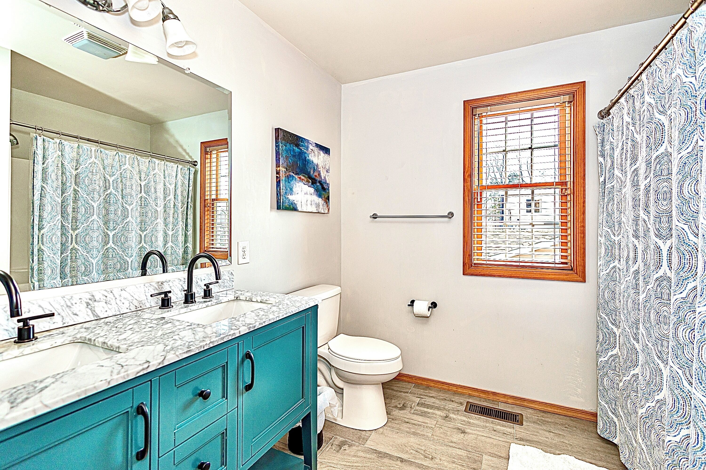 A bathroom with a marble sink, teal cabinets, a white toilet, and a shower curtain with a blue pattern.