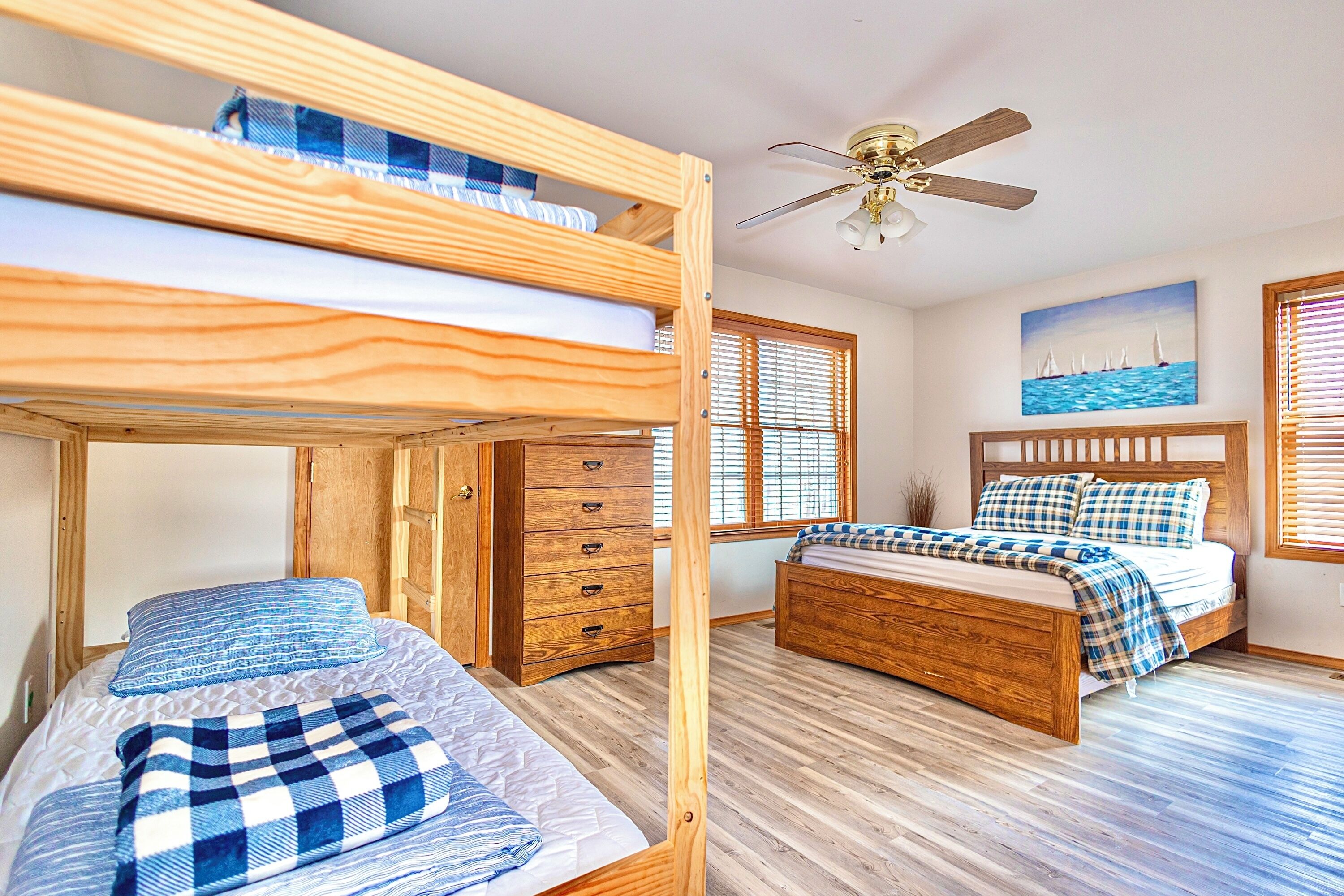 A bunk bed room with a ceiling fan, wooden furniture, and a painting of sailboats.