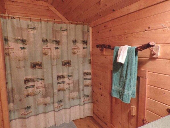 Baño de cabaña de madera con cortina de ducha temática náutica, un perchero con una toalla azul y una puerta de madera.