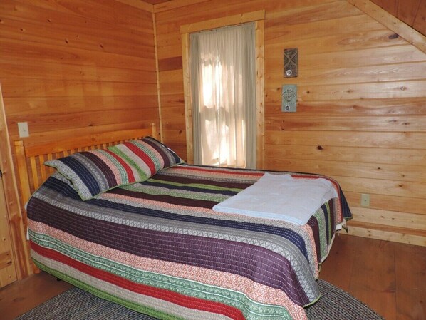 Un dormitorio de cabaña de madera con una cama, una ventana con cortinas y una pequeña decoración en la pared.