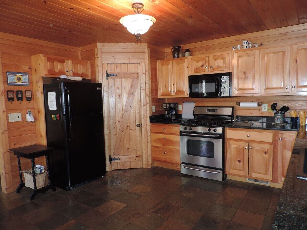 A wooden cabin kitchen with a refrigerator, stove, microwave, and wooden cabinets.