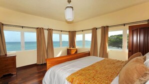 Une chambre avec un grand lit, une tête de lit en bois et une vue sur la mer.