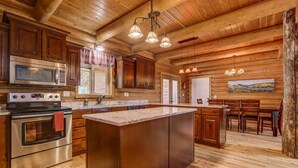 Una cocina con armarios de madera, una isla grande, electrodomésticos de acero inoxidable e iluminación colgante.