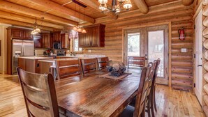 Interior espacioso de una cabaña de madera con una gran mesa de comedor, múltiples sillas, una cocina con electrodomésticos modernos y una acogedora chimenea.