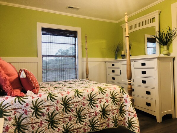 Un dormitorio con cama, cómoda, ventana con persianas y una planta.