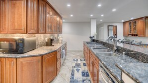 A modern kitchen with wooden cabinets, granite countertops, a built-in microwave, and a patterned rug. - OCEANFRONT LUXURY—Summer booking fast so Hurry and book!<br> (San Diego)