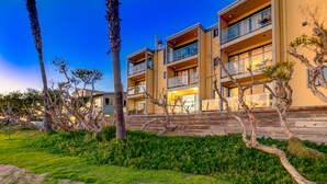 A multi-story building with balconies, a landscaped garden with trees, and a clear sky. - OCEANFRONT LUXURY—Summer booking fast so Hurry and book!<br> (San Diego)