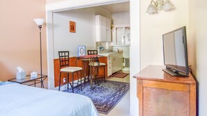 Een compacte hotelkamer met een bed, een klein bureau, een stoel, een televisie op een houten standaard, een kitchenette met kastjes, en een eethoek met een tafel en stoelen.