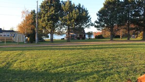 A grassy field with a house and trees in the background. - Grandview Beach Cottage, 3 brm , 2 baths, 10Km from S'side, Kayaks. (Miscouche)