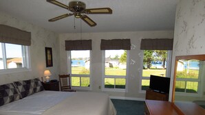 A bedroom with a bed, a ceiling fan, a dresser, a TV, and large windows with curtains. - Grandview Beach Cottage, 3 brm , 2 baths, 10Km from S'side, Kayaks. (Miscouche)