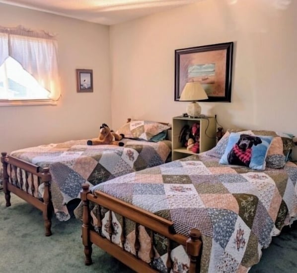 A bedroom with two wooden beds, a window with curtains, a lamp, and a framed picture on the wall.