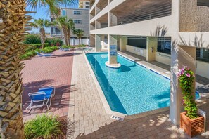 A swimming pool with lounge chairs and a no diving sign, surrounded by a brick patio and palm trees.