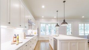 A kitchen with white cabinetry, a central island, pendant lighting, and a view of the outdoors through large windows. - Beautiful New Construction Home in Buckhead! Convenience & Luxury! (Atlanta)