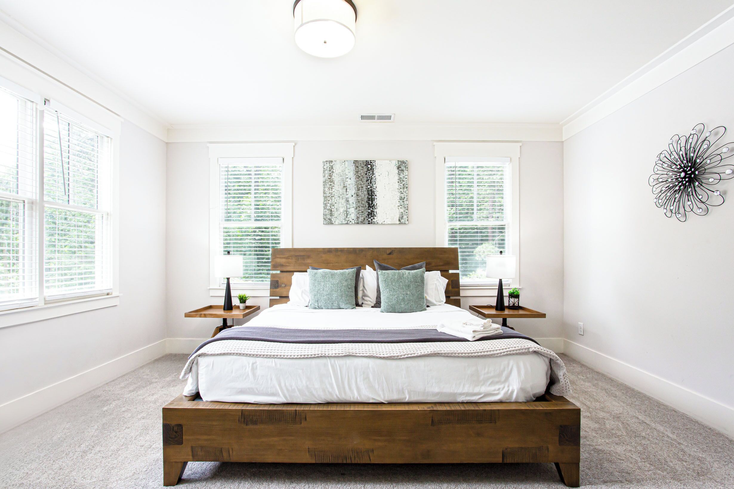 Un dormitorio con una cama de madera, dos mesitas de noche, una obra de arte en la pared y una ventana con persianas.