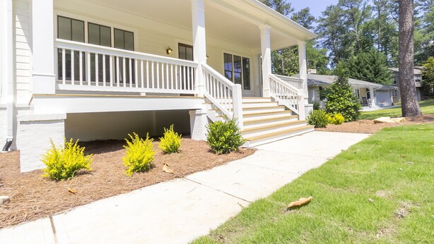 A two-story house with a covered porch, a front yard with small shrubs, and a visible staircase leading to the second floor. - Beautiful New Construction Home in Buckhead! Convenience & Luxury! (Atlanta)