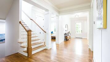 A spacious hallway with hardwood floors, white walls, and a wooden staircase.