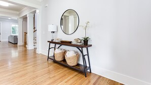 A hallway with a wooden floor, a console table with baskets, a mirror, and a potted plant. - Beautiful New Construction Home in Buckhead! Convenience & Luxury! (Atlanta)