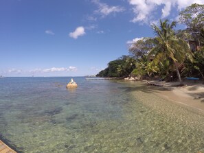 A clear tropical beach with a statue in the water, palm trees, and a wooden dock.