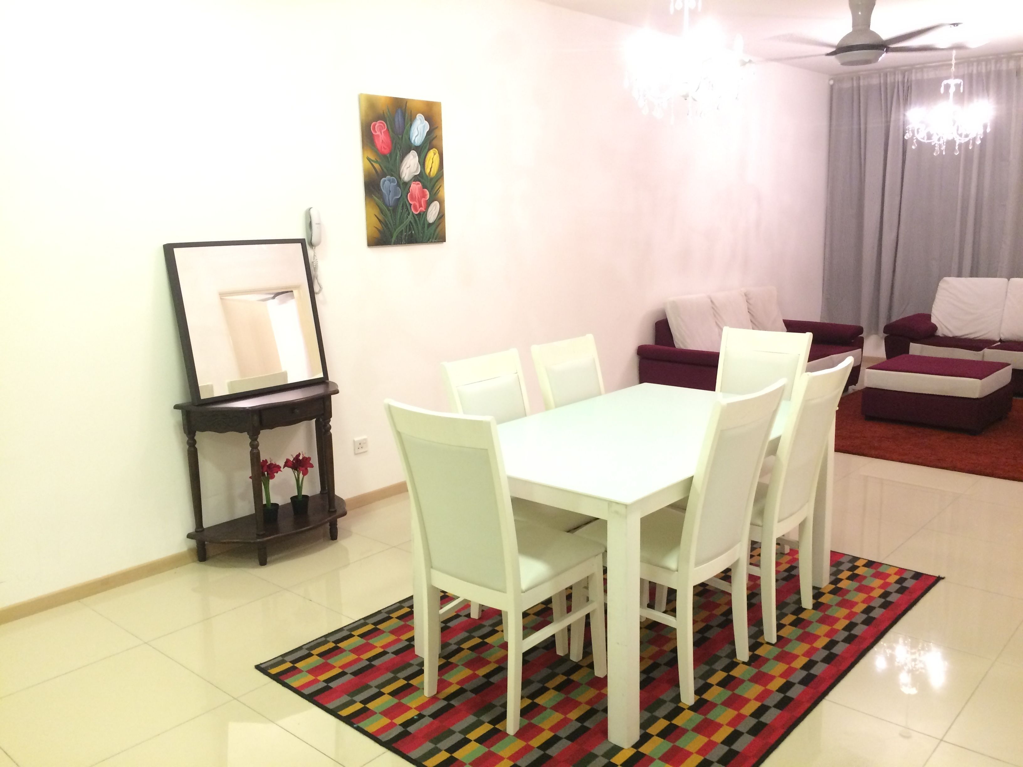 Un comedor con una mesa y sillas blancas, un tapete colorido, un cuadro en la pared y un ventilador de techo.