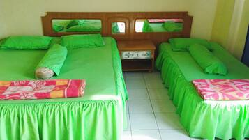 A room with two beds, each with green bedding and a wooden headboard. There is a small table between the beds.