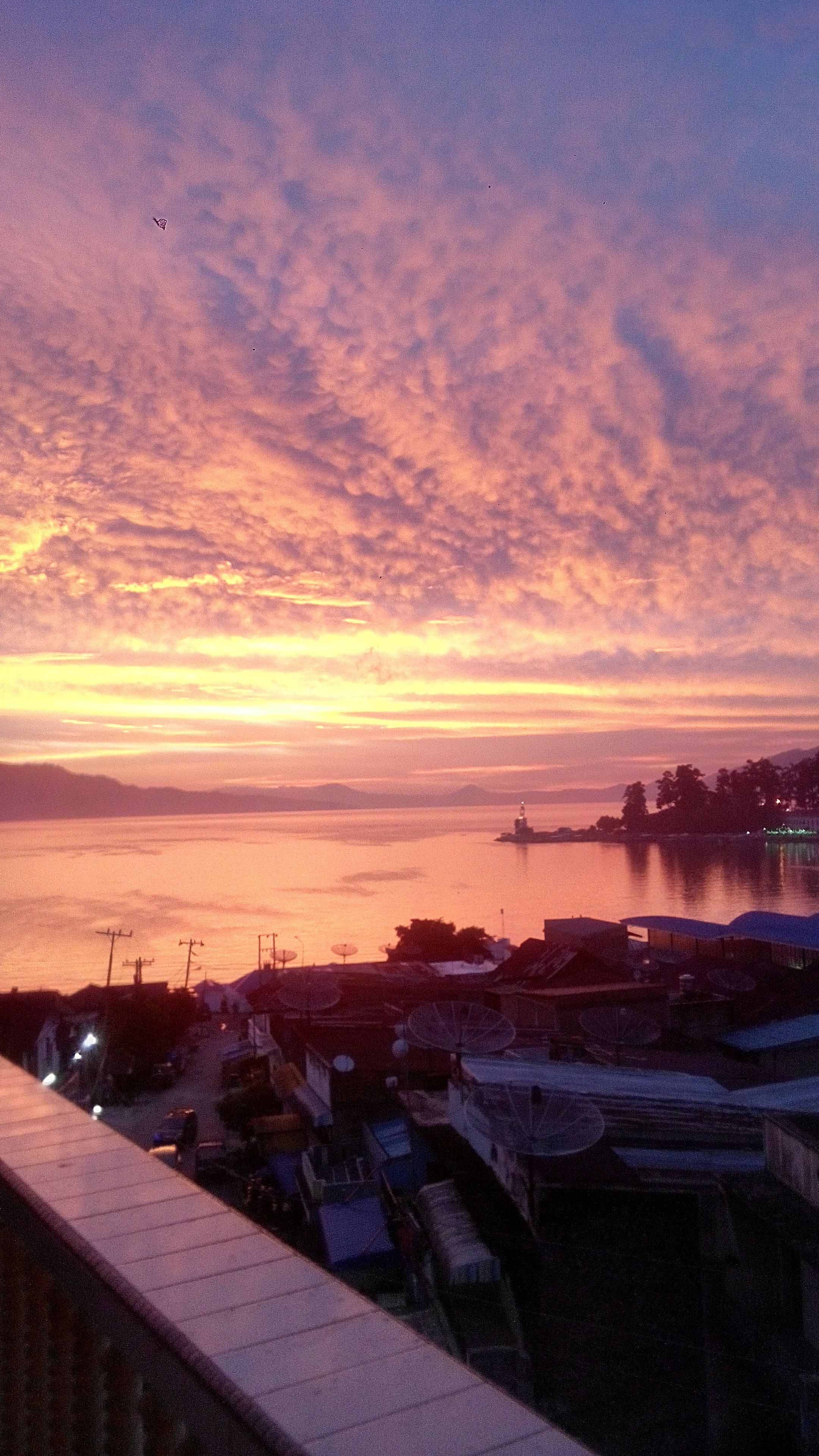 A coastal cityscape at sunset with a lighthouse in the distance.