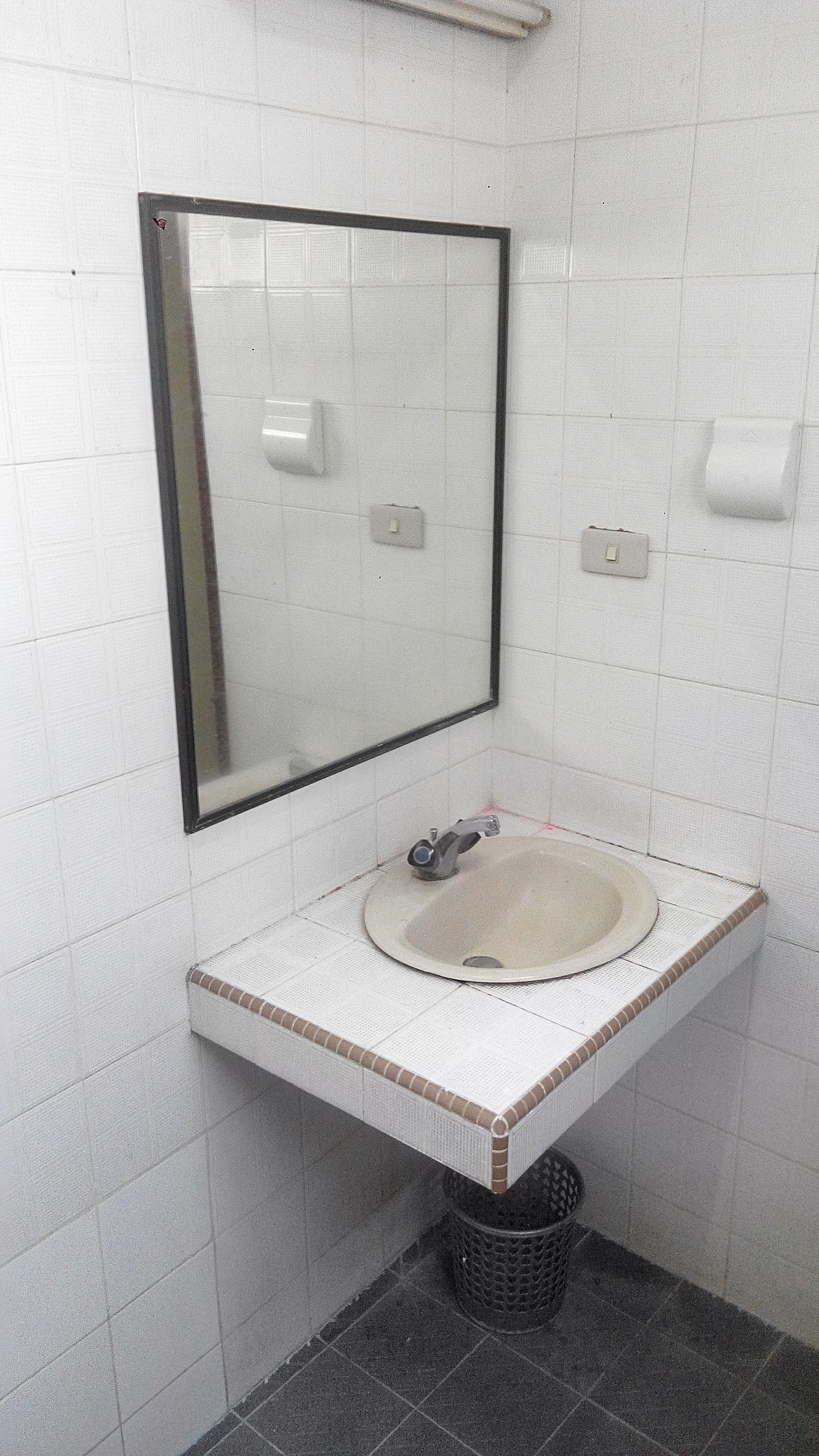 A small bathroom with a white sink, a mirror, and a trash bin.