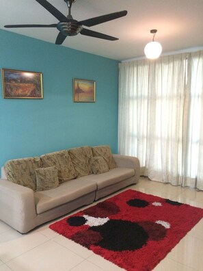 Ein Wohnzimmer mit einem beige farbenen Sofa, einem Teppich mit roten und schwarzen Mustern, einem Deckenventilator und zwei gerahmten Bildern an der Wand.