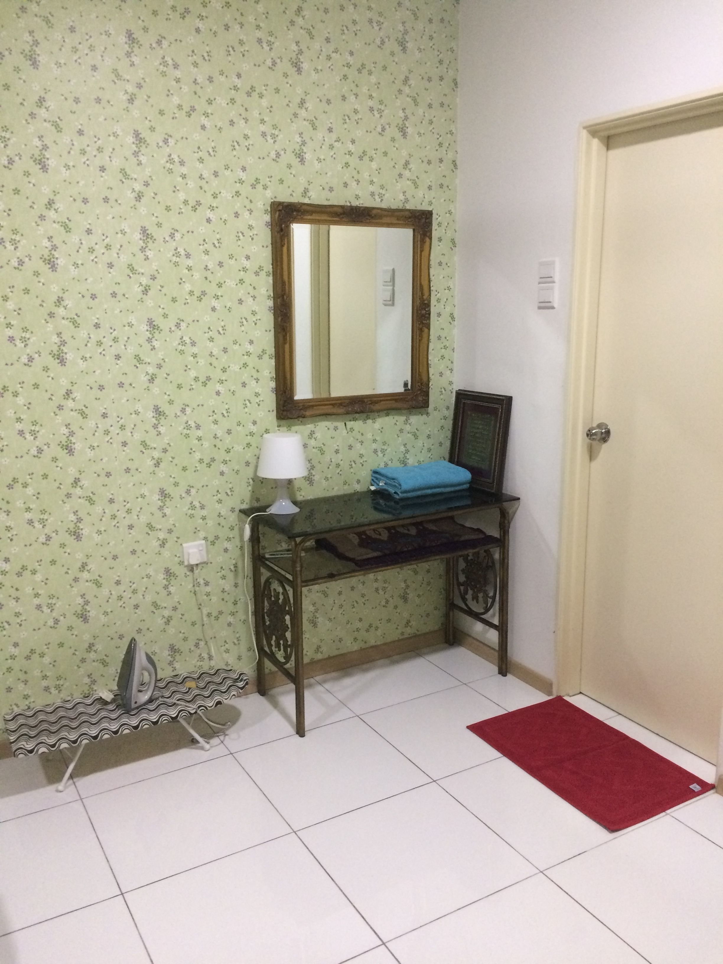 A bathroom with floral wallpaper, a mirror, a sink with a towel, an iron, and a red rug.