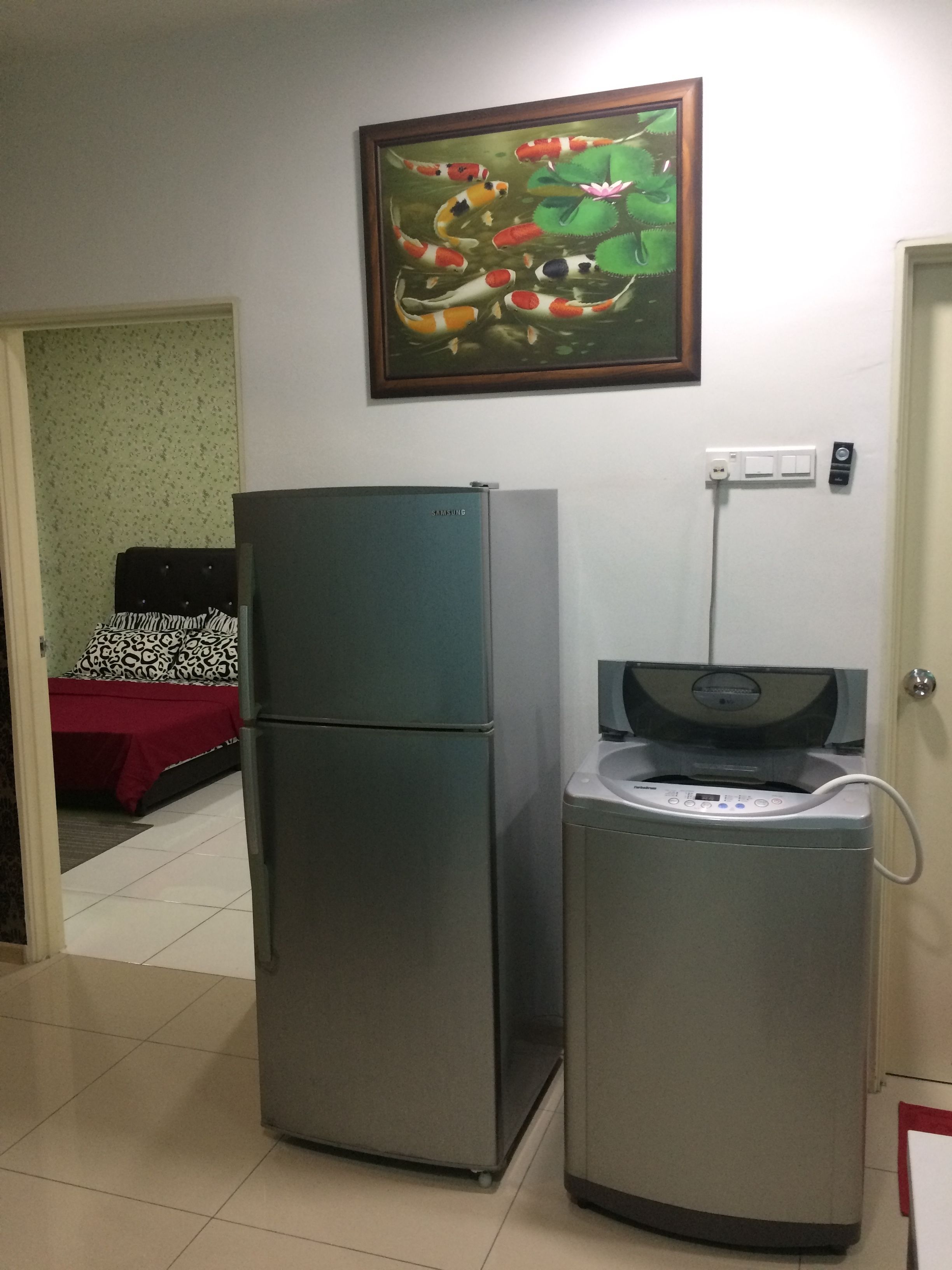 A compact kitchen with a refrigerator, a washing machine, and a painting of koi fish on the wall.