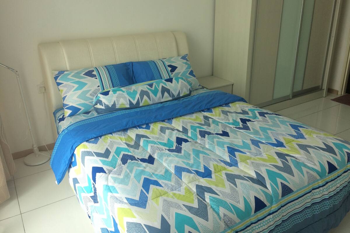 Ein Bett mit einem gemusterten Überwurf und Kissen, ein weißes Kopfteil und ein gefliestes Badezimmer.
