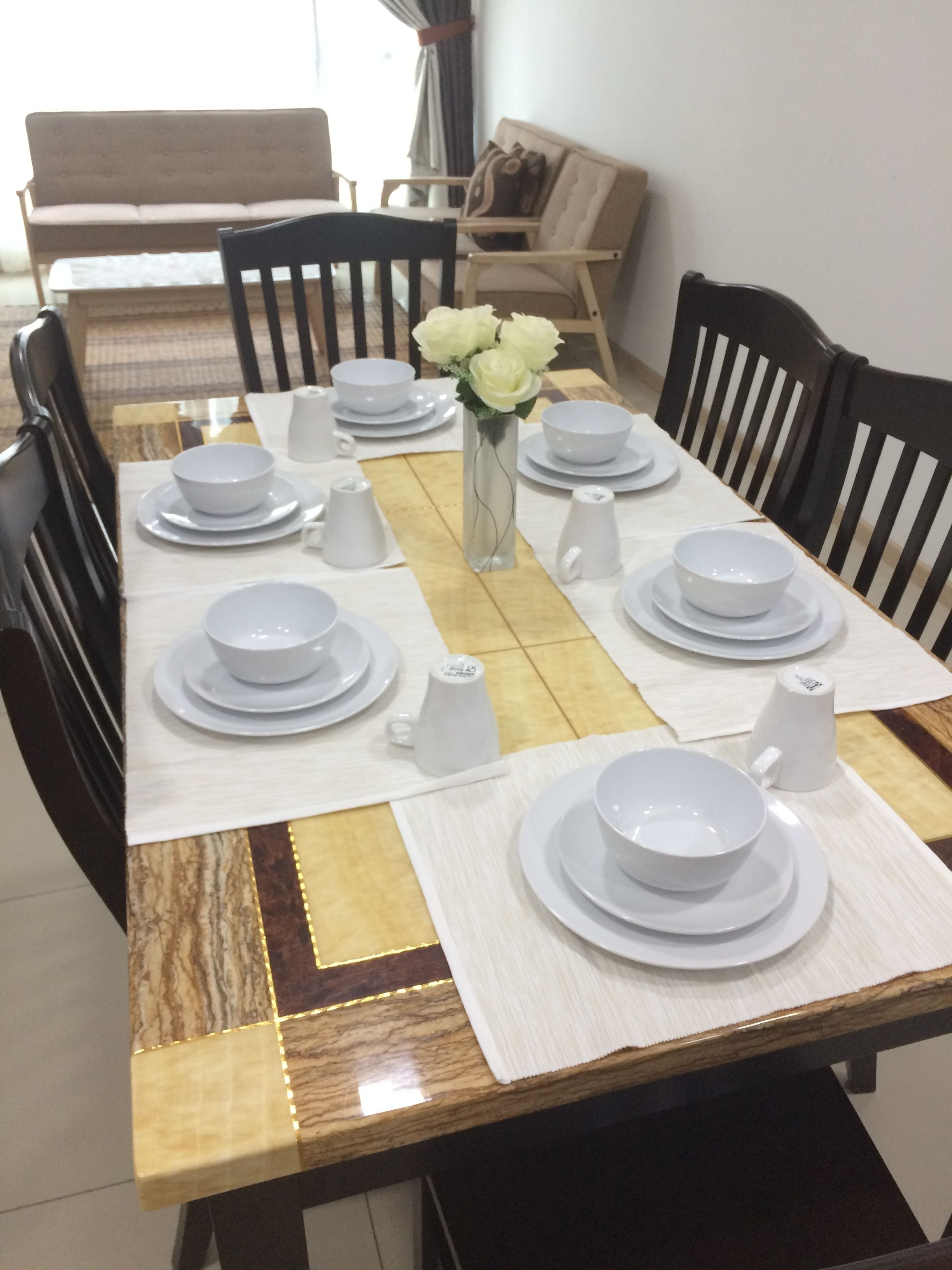 Une table à manger dressée avec de l’assiette, des bols et des tasses blancs, entourée de chaises noires.