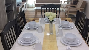 A dining area with a table set for four, a sofa, and a TV in the background. - Lawang Suite 2 Bedroom Standard Apartment 2 (Shah Alam)