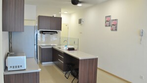 A modern kitchen with a built-in microwave, a stove, and a sink. There are two stools and a small island with a sink. The kitchen has wooden cabinets and a white countertop. - Lawang Suite 2 Bedroom Standard Apartment 2 (Shah Alam)