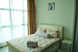 A neatly made bed with a patterned bedspread and pillows, a bedside table with a lamp, and a window with curtains. - Lawang Suite 2 Bedroom Standard Apartment 3 (Shah Alam)