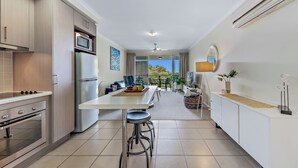 A modern kitchen with stainless steel appliances, a dining area with stools, and a view of the outdoors. - Alpha 8 on Waterson - Airlie Beach (Airlie Beach)