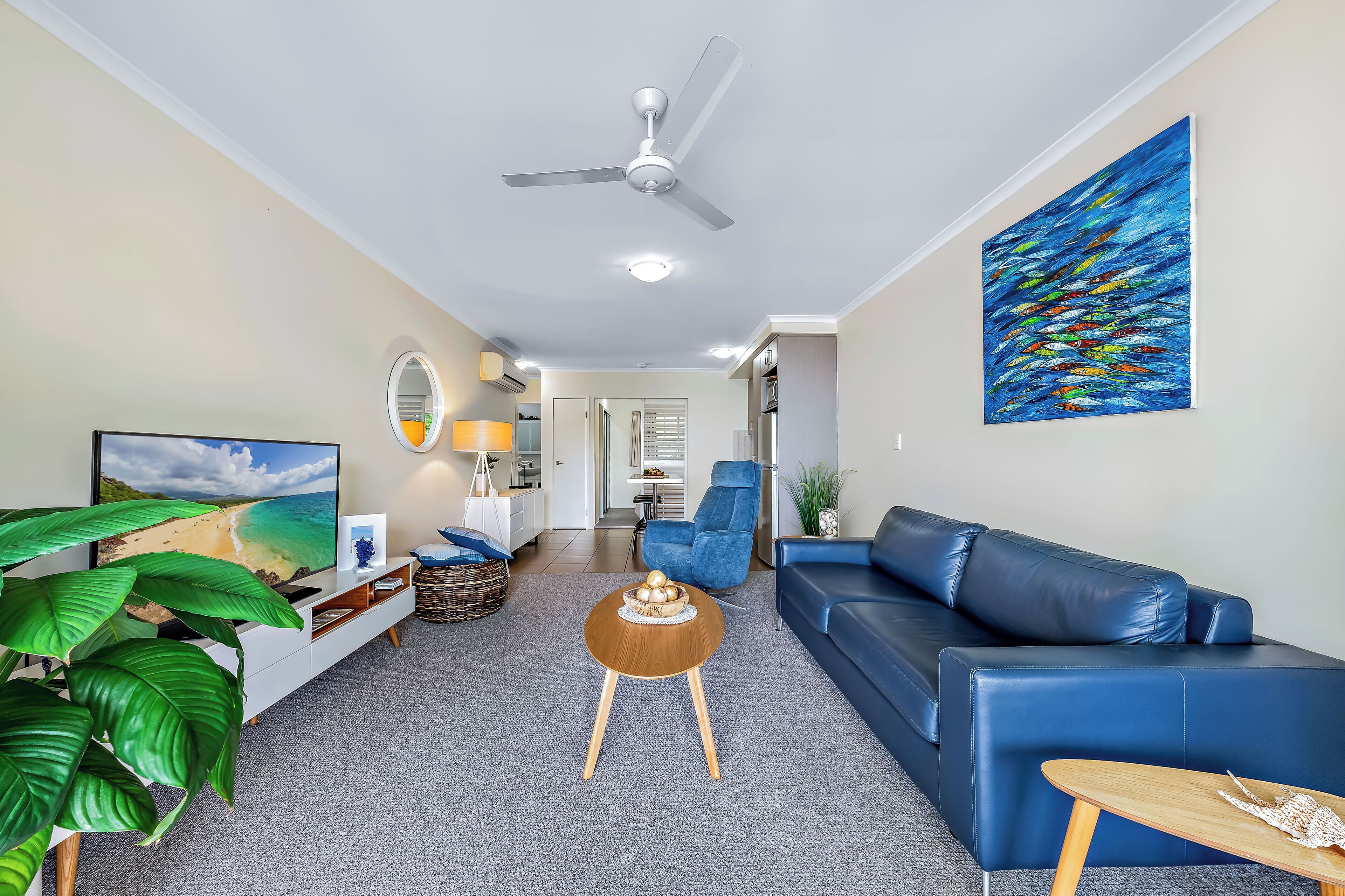 A modern living room with a blue sofa, a wooden coffee table, and a large painting of fish on the wall.