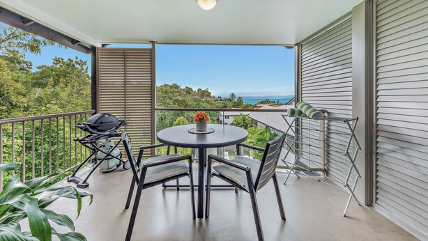 A balcony with a round table, chairs, a grill, and a view of the ocean. - Alpha 8 on Waterson - Airlie Beach (Airlie Beach)