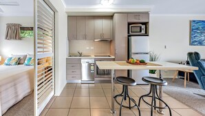 A compact kitchen with modern appliances, a dining area with stools, and a view of the outdoors. - Alpha 8 on Waterson - Airlie Beach (Airlie Beach)
