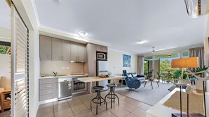 A modern kitchen with a dining area, a bar stool, and a view of the outdoors. - Alpha 8 on Waterson - Airlie Beach (Airlie Beach)