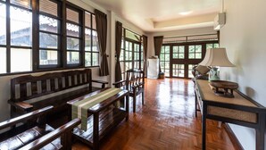A spacious room with wooden flooring, large windows, a bench, a table, and a refrigerator. - Doi Inthanon Riverside Resort (Wiang Nong Long)
