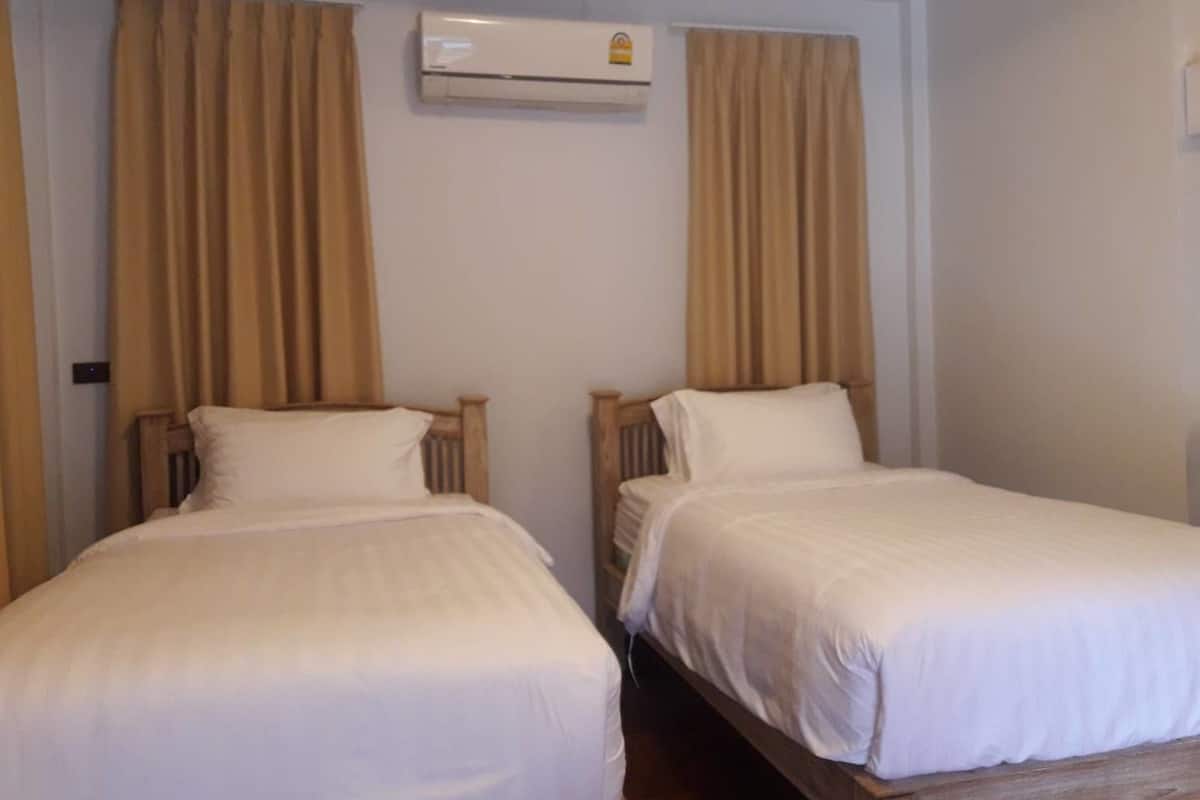 Two single beds with wooden headboards, beige curtains, and an air conditioning unit on the wall.