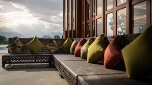 A wicker sofa with colorful cushions, positioned near a large window overlooking a scenic landscape. - Doi Inthanon Riverside Resort (Wiang Nong Long)