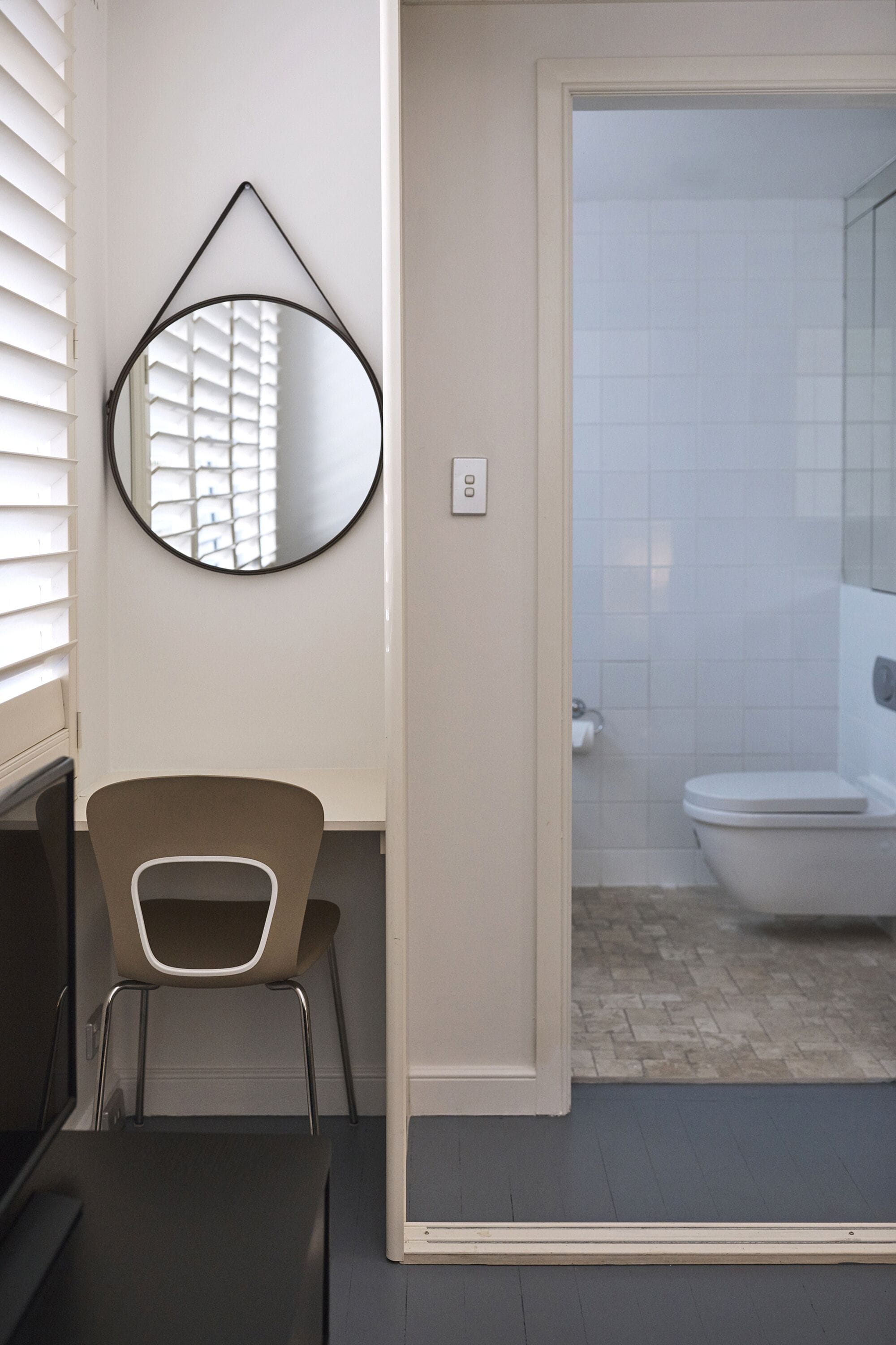 A modern bathroom with a toilet, a mirror, and a chair.