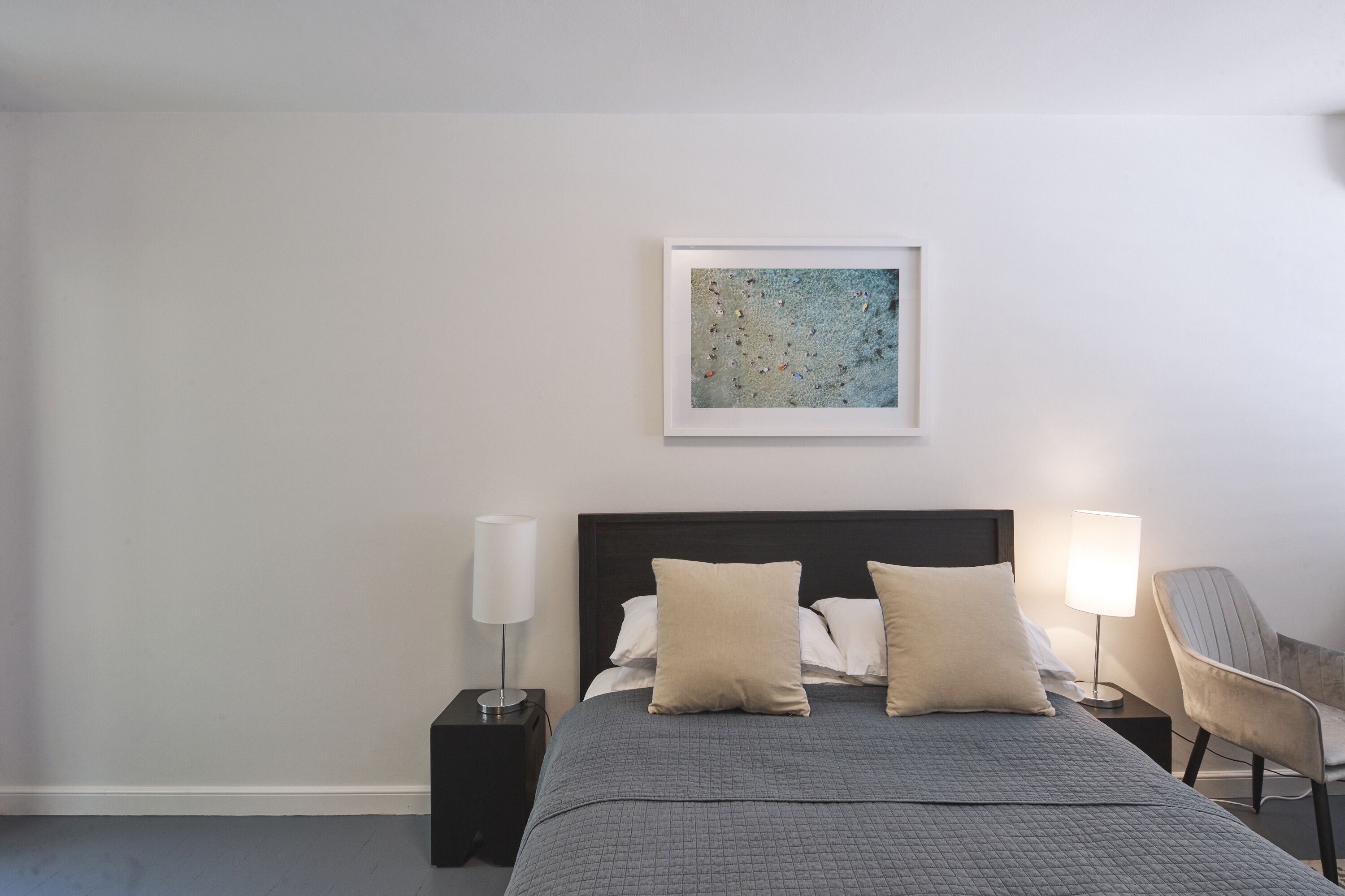 A neatly arranged hotel room with a bed, two bedside tables, a chair, and a framed artwork on the wall.