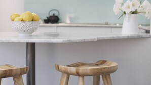 Una cocina con cubierta blanca, un cuenco de limones, un florero con flores blancas y taburetes de madera.
