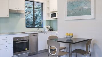 A modern kitchen with white cabinets, a glass dining table, and a window with a view of trees.