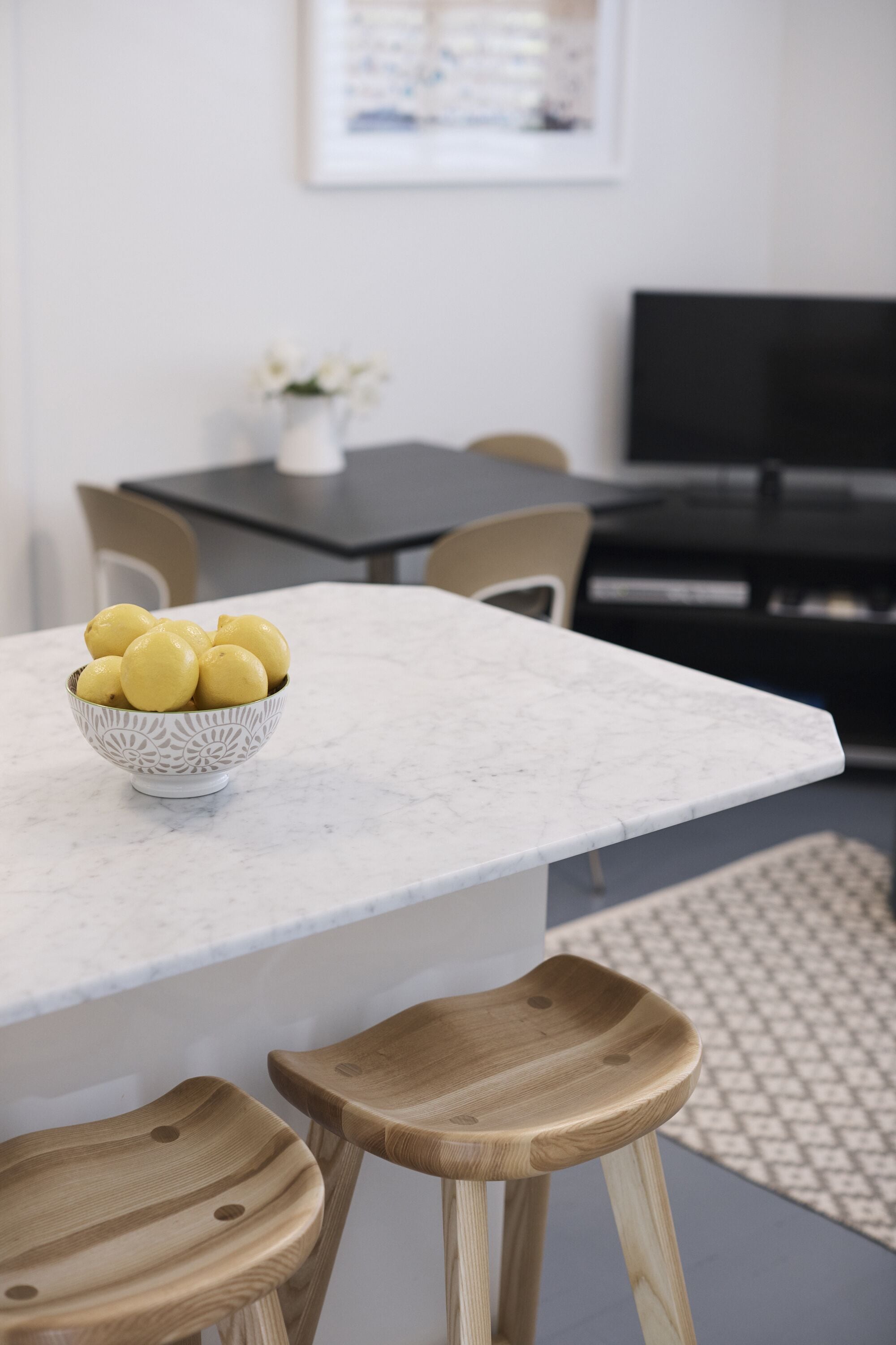 A kitchen with a marble countertop, wooden stools, and a bowl of lemons.