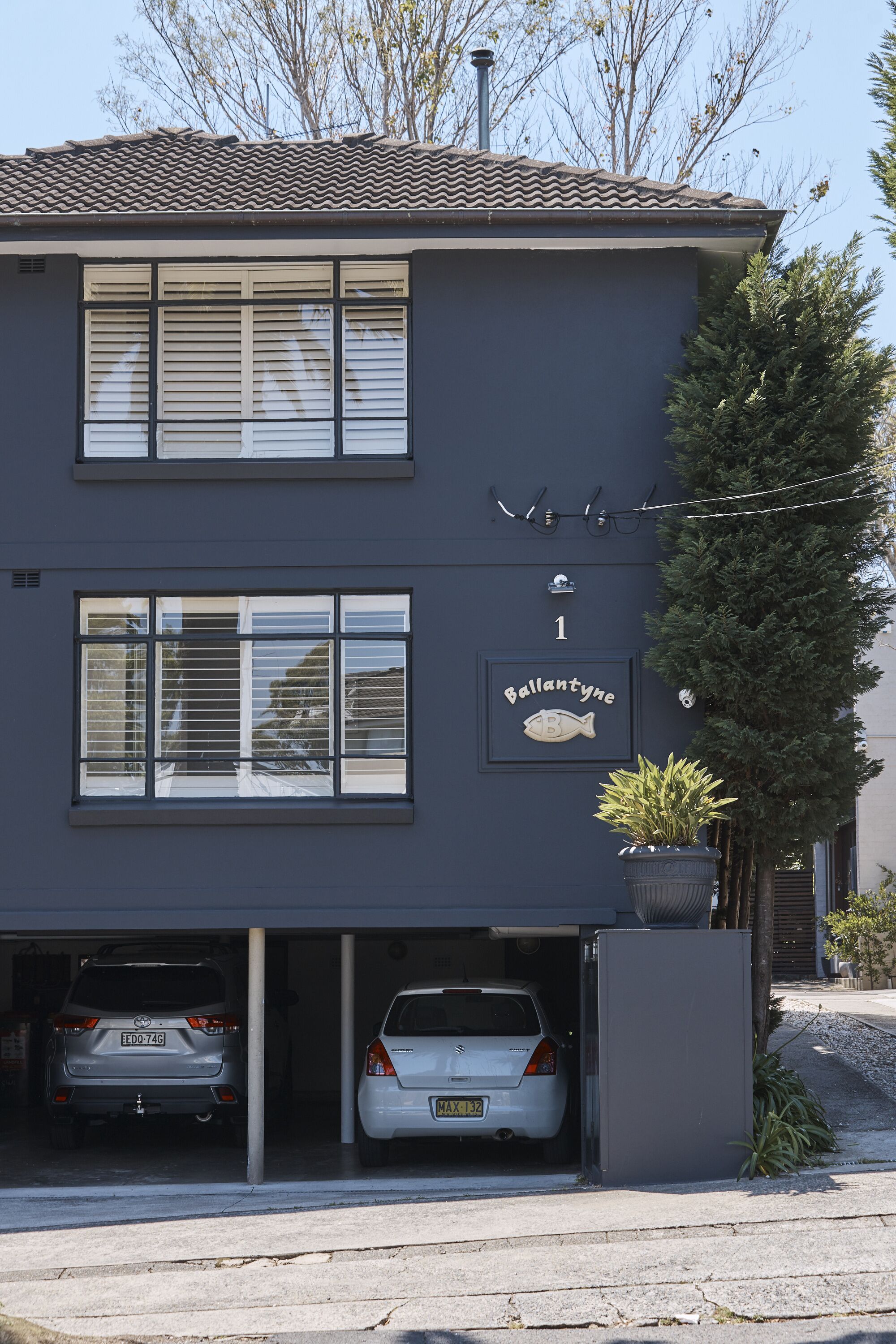 A two-story building with a dark facade, a fish-shaped sign, and two cars parked in a garage.